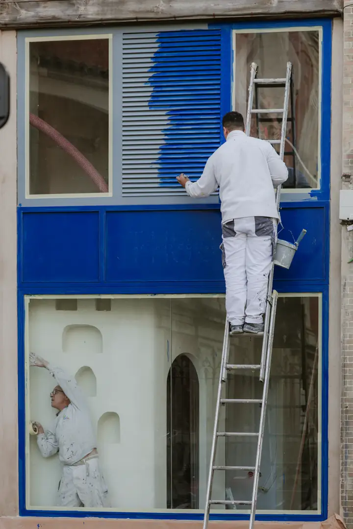 Maler auf der Leiter streicht eine Fassade blau