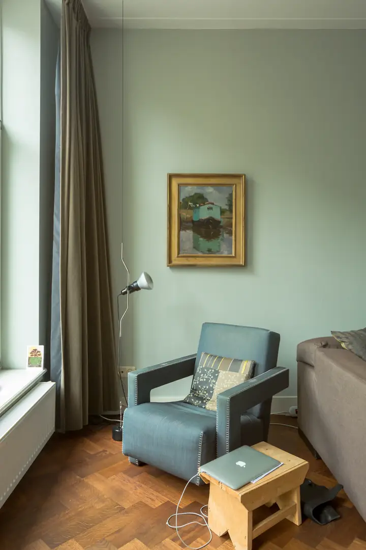 Wohnzimmer mit salbeigrüner Wand und Sessel am Fenster