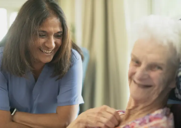 Pflegerin und ältere Patientin lachen gemeinsam